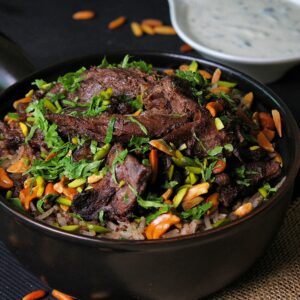 A delicious serving of spiced meat with rice, nuts, and herbs in a bowl.